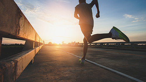 Läufer läuft dem Sonnenuntergang entgegen und symbolisiert damit eine lange Laufzeit